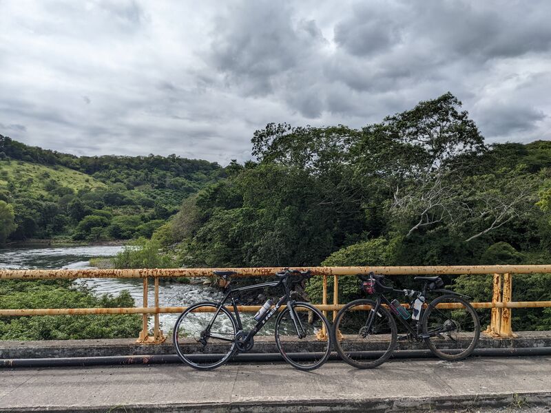 Dos bicicletas recargadas en el barandal de un puente. Detrás se aprecia un gran río y muchísima vegetación alrededor.